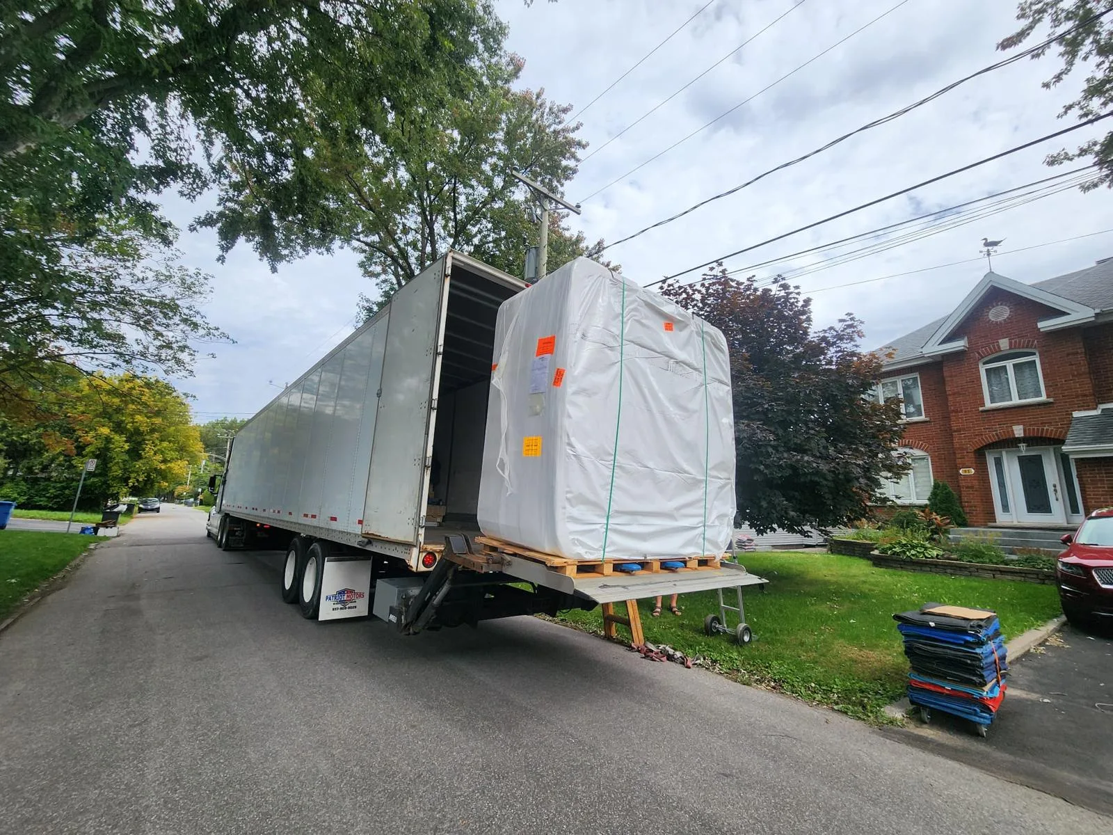 A crated shipment on a Klacar liftgate at a house, blanket-wrapped and ready to go inside